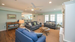 Un salon avec deux canapés, une table basse et une lampe. On y trouve également un ventilateur de plafond et une porte portant l’inscription « Anna Maria Island ».