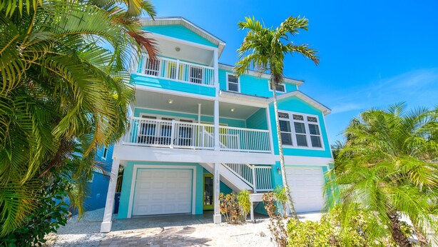 Une maison à deux étages, avec une façade blanche et turquoise, un garage à l’avant et une allée menant à l’entrée.
