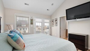 A bedroom with a large bed, a dresser, a TV mounted on the wall, and a balcony door. - 4BR Townhouse with Garage & Pool in Downtown OC- Close to Beach & Boardwalk! (Ocean City)