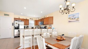 A kitchen with wooden cabinets, a refrigerator, and a dining area with white chairs and a wooden table. - 4BR Townhouse with Garage & Pool in Downtown OC- Close to Beach & Boardwalk! (Ocean City)