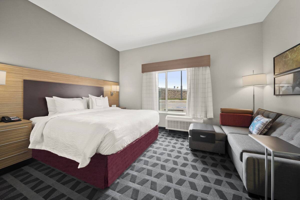 Ein Hotelzimmer mit einem großen Bett, einer Couch, einem Schreibtisch und einem Fenster mit Vorhängen.
