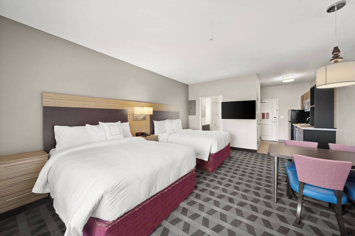 Ein Hotelzimmer mit zwei Betten, einem Schreibtisch, einem Stuhl und einer Küchenzeile.