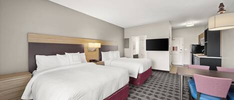 A hotel room with two beds, a desk, a chair, and a kitchenette.