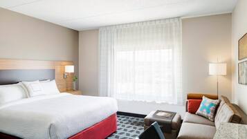 A hotel room with a large bed, a sofa, a small table, and a window with sheer curtains.