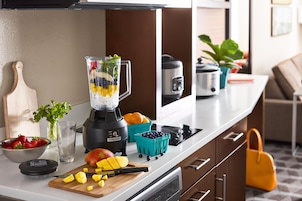 Una encimera de cocina con una licuadora, una tabla de cortar con fruta, un bol de fresas y una planta en maceta.