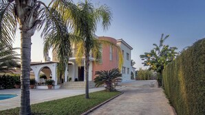 Una villa con piscina, palmeras y un césped bien cuidado.