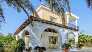 Una villa de dos pisos con un patio cubierto, mobiliario exterior y plantas en macetas.