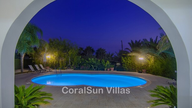 Una piscina en CoralSun Villas con sillas de descanso y plantas tropicales.