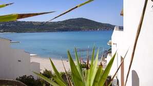 Une vue côtière avec une plage, une mer bleue et limpide, et une colline en arrière-plan.