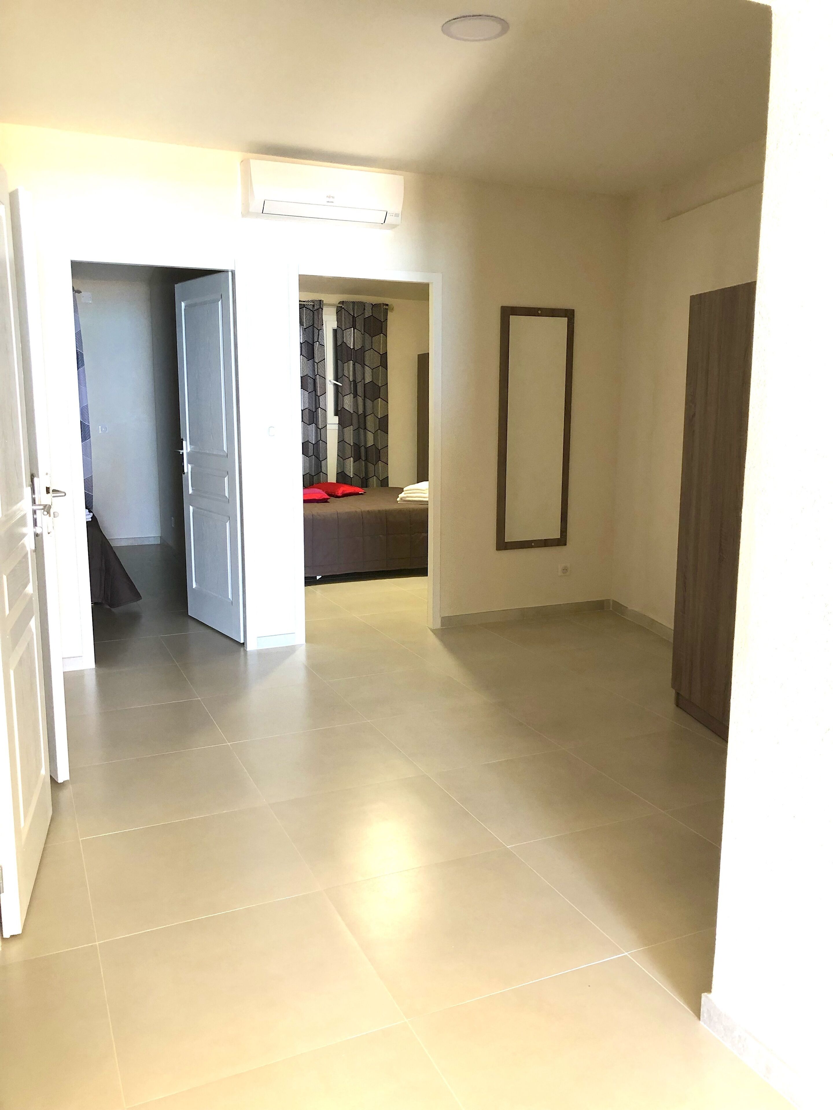 A hallway with a bed, a mirror, and a door leading to another room.