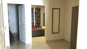 A hallway with a bed, a mirror, and a door leading to another room.