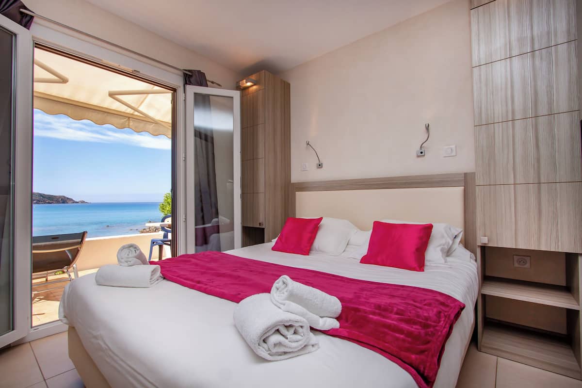 Een hotelkamer met een bed, een balkon met uitzicht op zee en een schuifdeur naar het balkon.