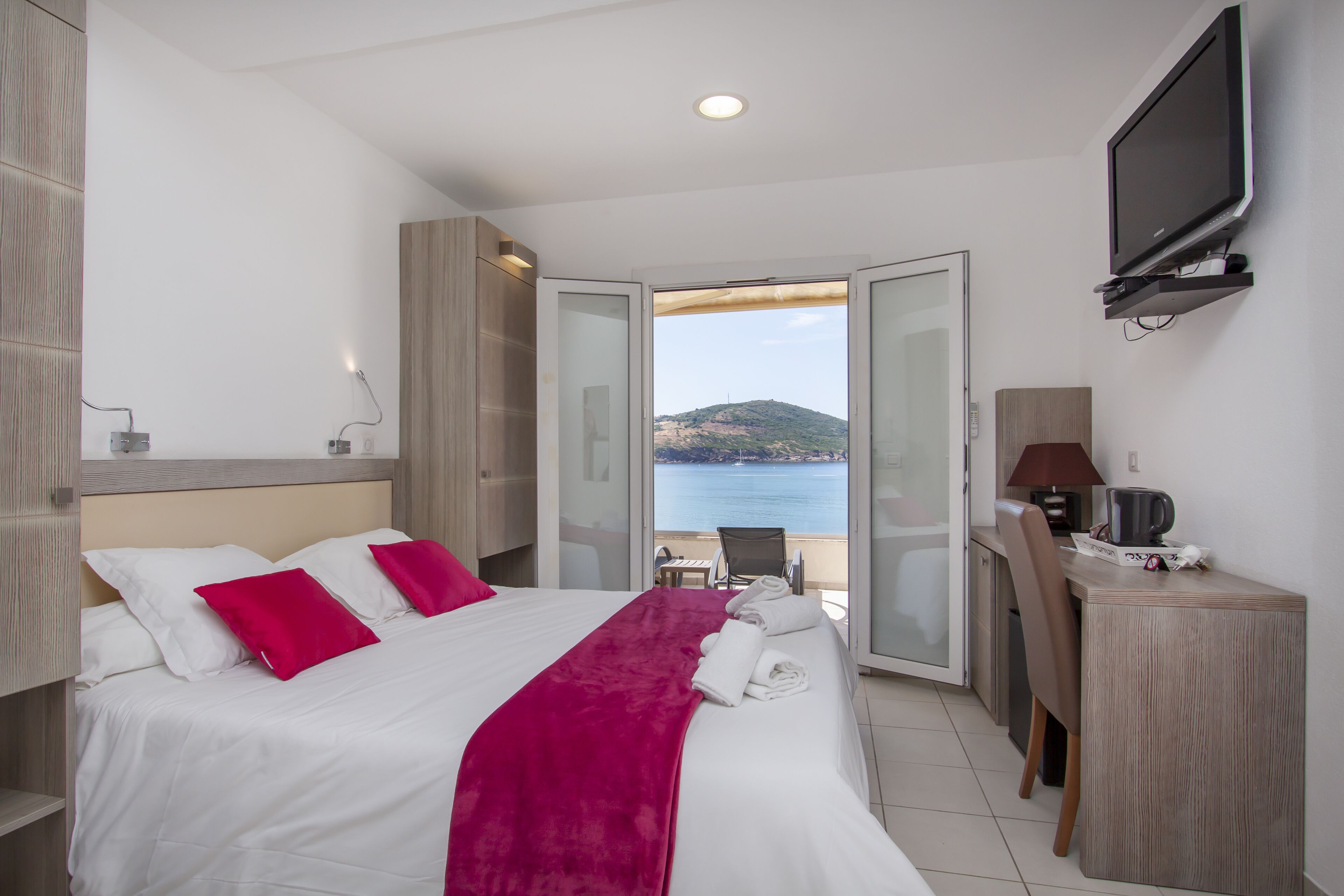 Een hotelkamer met een bed, een bureau, een stoel, een televisie en uitzicht op zee.