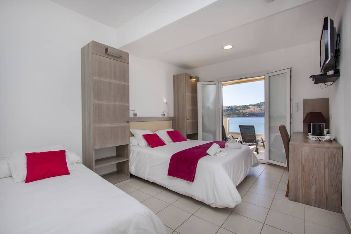 Een hotelkamer met twee bedden, een bureau, een stoel, een televisie en uitzicht op zee.