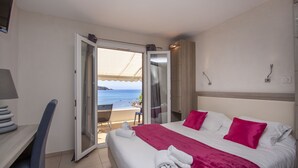 Une chambre d’hôtel avec un lit, un bureau et une chaise. On peut admirer la plage et l’océan à travers une porte ouverte.