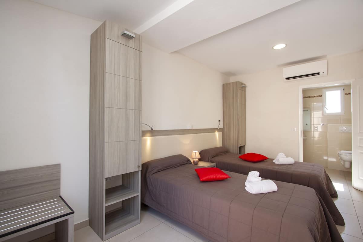 Een hotelkamer met twee bedden, een bankje, een kledingkast en een badkamer.