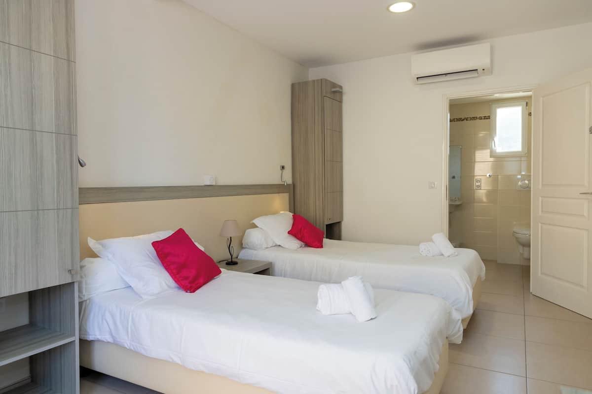 Hotelkamer met twee bedden, een garderobe, een airconditioning en een badkamer door een open deur zichtbaar.