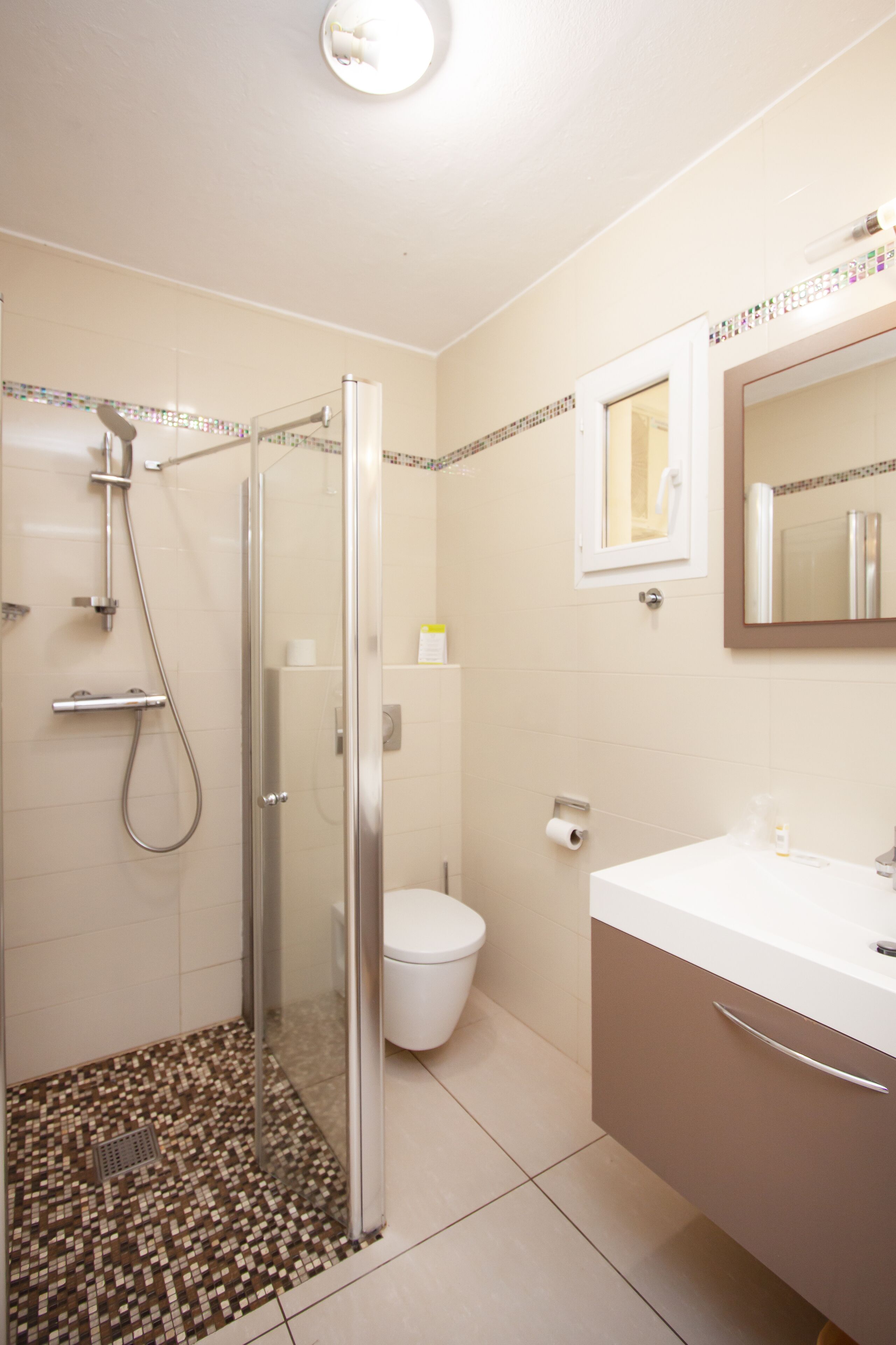 A bathroom with a glass-enclosed shower, a toilet, and a sink with a mirror above it.
