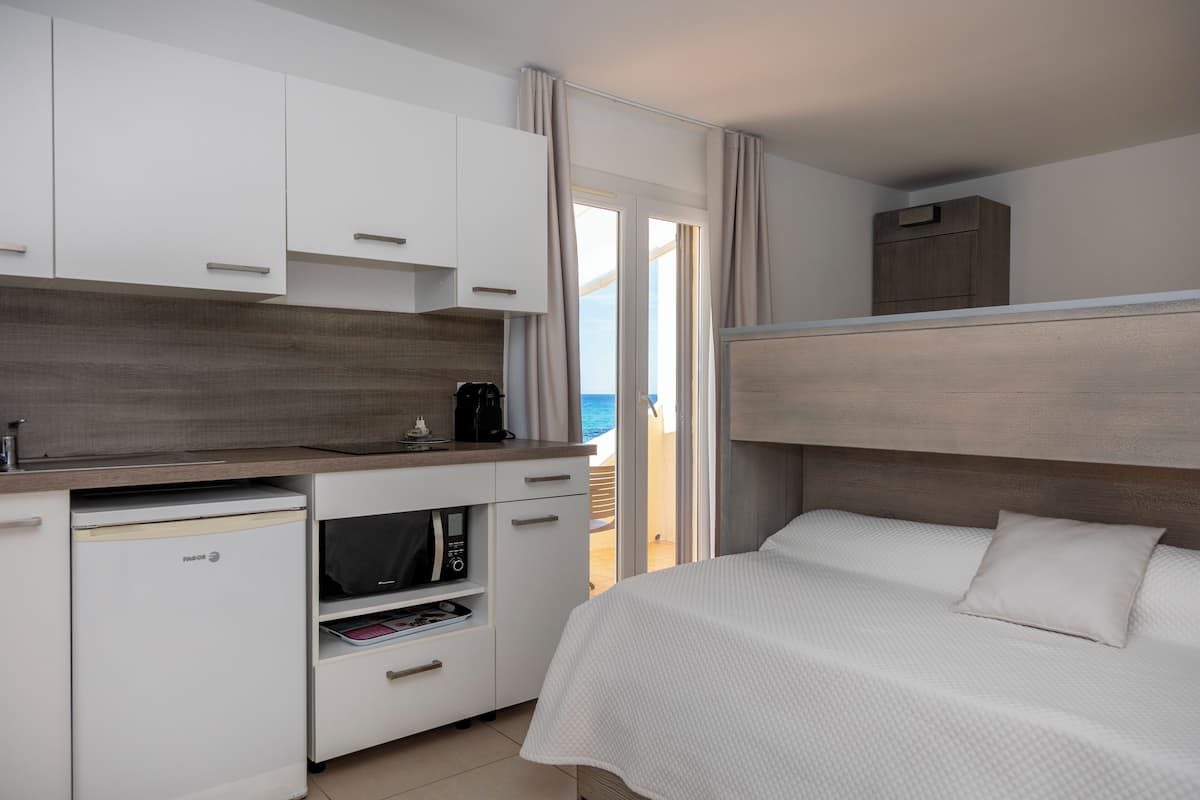 Een compacte hotelkamer met kitchenette, een bed en uitzicht op zee.