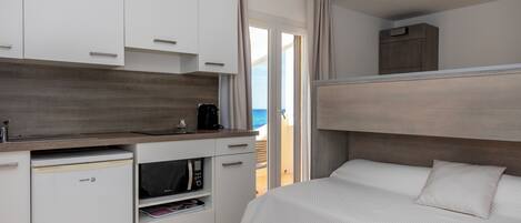 A compact hotel room with a kitchenette, a bed, and a view of the sea.