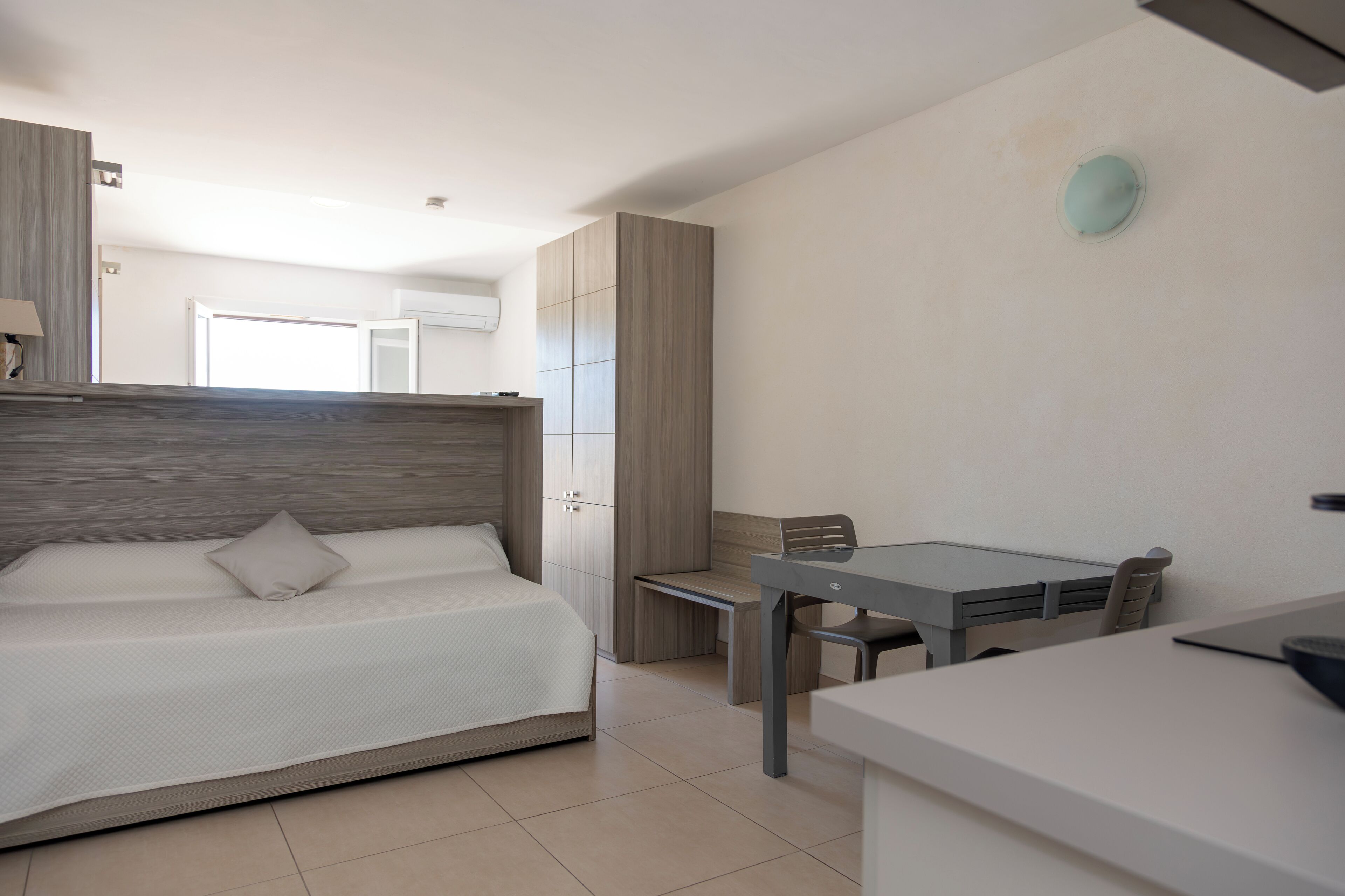 Une chambre moderne avec un lit, un bureau et une chaise. On y trouve également une armoire et une fenêtre donnant sur un beau paysage.