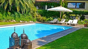 A swimming pool with a wooden deck, surrounded by lush greenery and a house with a tiled roof. - Le Grotte Cottage with Pool Elba Island (Portoferraio)