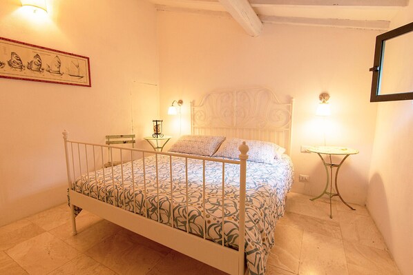 A bedroom with a bed, a chair, a table, and a wall-mounted lamp. - Le Grotte Cottage with Pool Elba Island (Portoferraio)