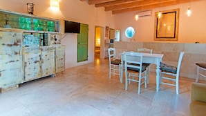 A dining area with a white table and chairs, a rustic cabinet, and a green door. - Le Grotte Cottage with Pool Elba Island (Portoferraio)