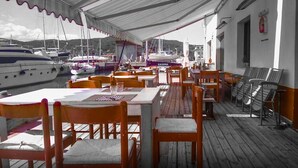 A covered outdoor dining area with wooden tables and chairs, overlooking a marina with boats. - Le Grotte Cottage with Pool Elba Island (Portoferraio)