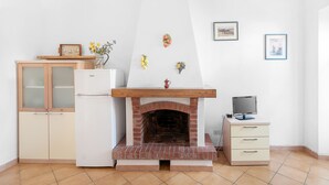 A kitchen with a brick fireplace, a refrigerator, a wooden cabinet, and a small desk with a computer. - Apartment The triangle near the center and the beach (Marina di Campo)