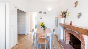 A dining area with a wooden table and chairs, a tiled backsplash, and a brick fireplace. - Apartment The triangle near the center and the beach (Marina di Campo)