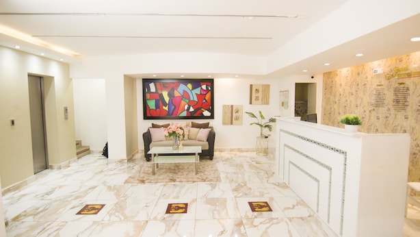 Un hall d’hôtel comprenant un comptoir d’accueil, un canapé avec des coussins, une table basse ornée de fleurs et un grand tableau abstrait accroché au mur.