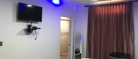 A bedroom with a bed, a TV mounted on the wall, a mirror, and a ceiling light.