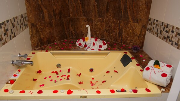 A bathtub with rose petals and a towel with a heart design. - Hotel Gold Premium (Bonao)