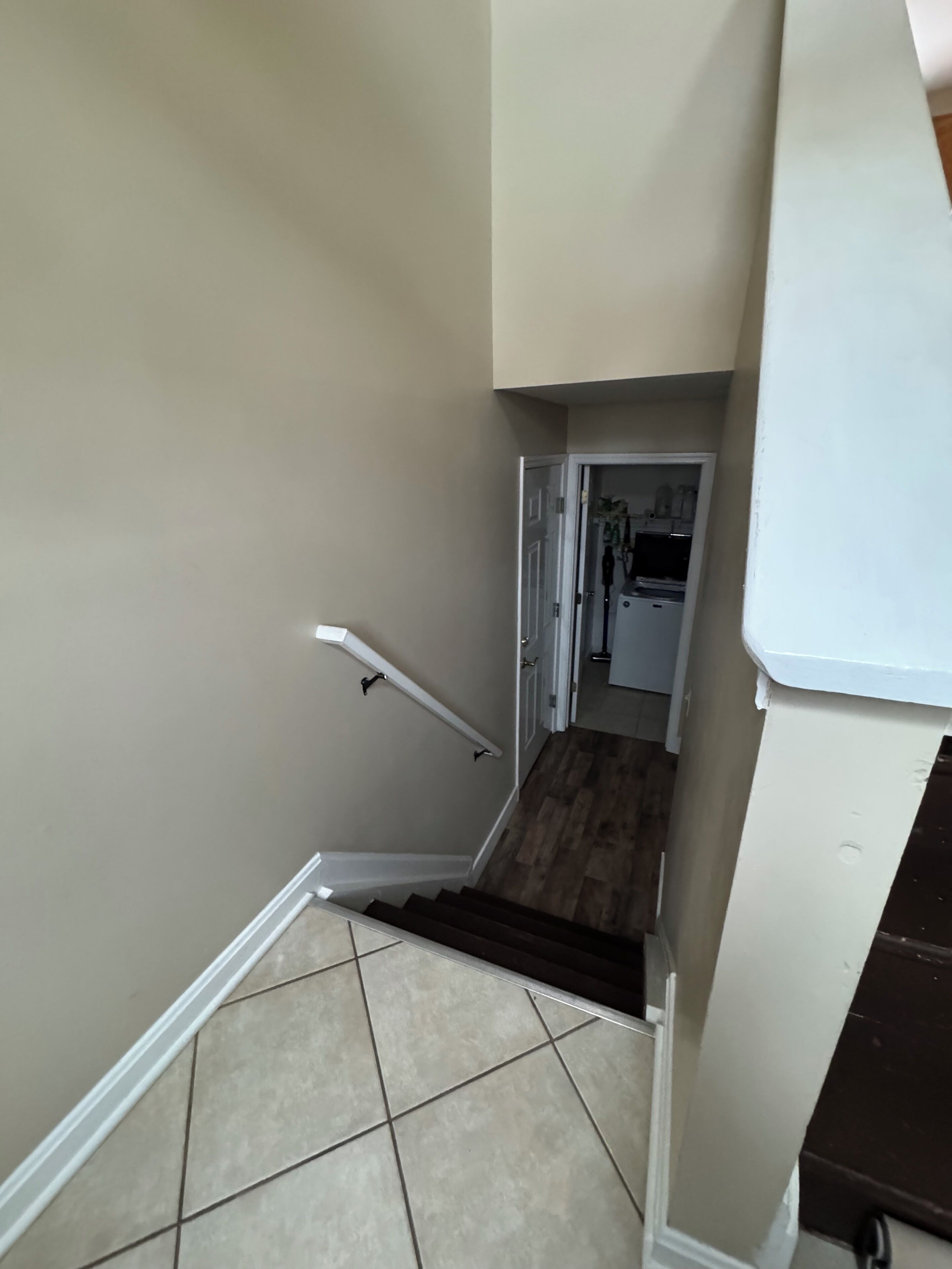 Una escalera con barandilla, paredes color beige y piso de baldosas que conduce a una puerta.