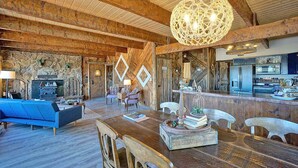 A rustic interior with exposed wooden beams, a stone fireplace, a blue sofa, a wooden dining table, and a kitchen area. - Charming Mountain Chalet with Stunning Views (Montrose)