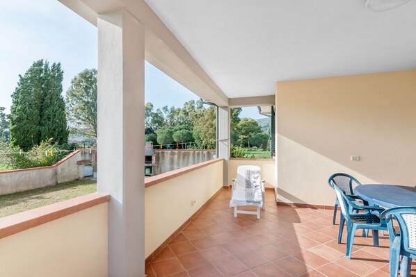 A balcony with a table and chairs, a view of greenery, and a white wall.