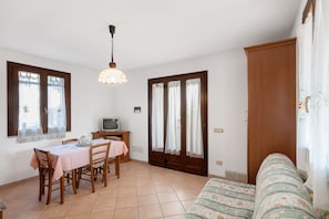 A room with a dining table, chairs, a television, and a sofa.