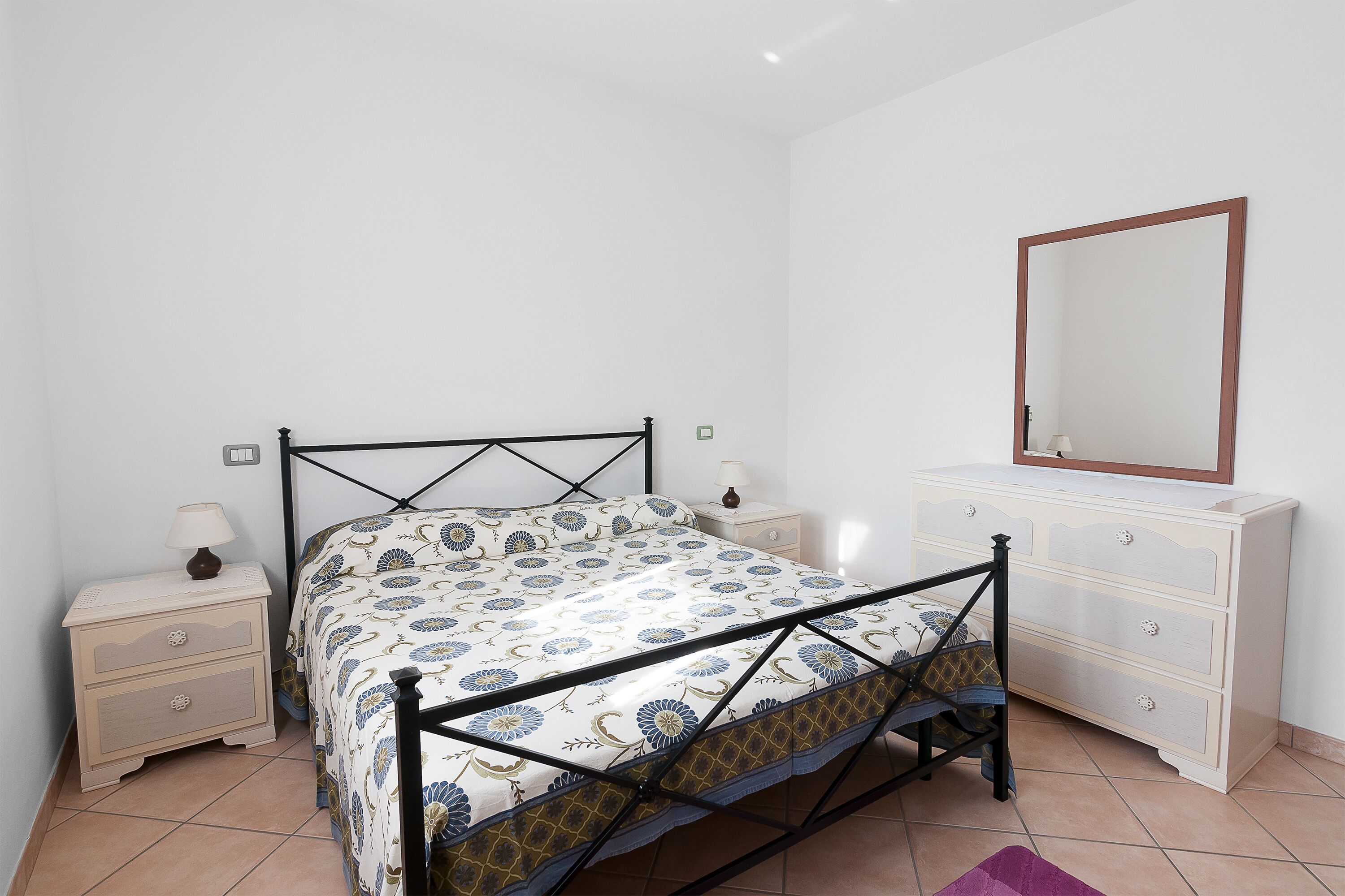 Una camera da letto con un letto, comodini, una cassettiera e uno specchio.