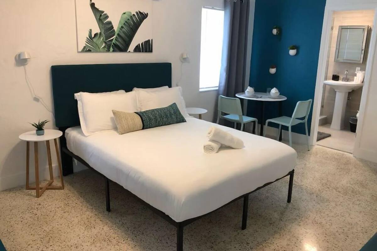 Een hotelkamer met een bed, een tafeltje met stoelen, een wastafel en een spiegel.
