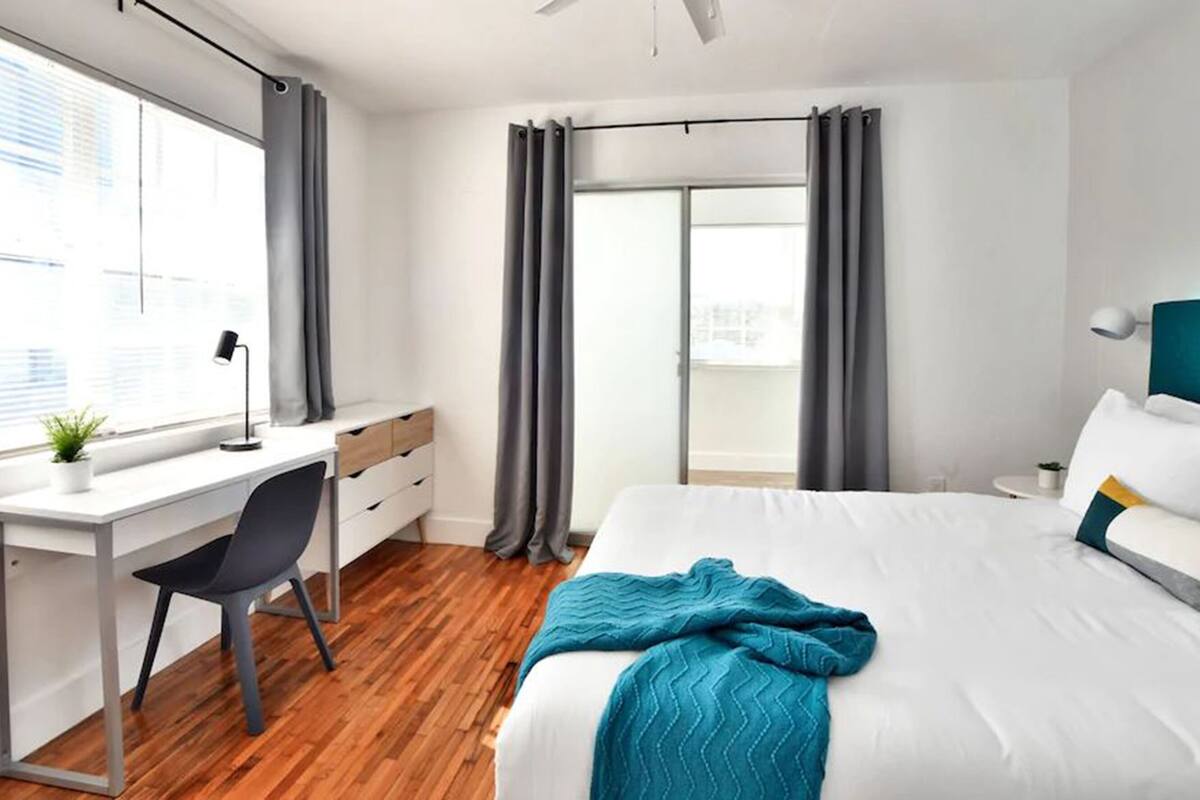 Een moderne slaapkamer met een bureau, stoel en een bed met een blauwe deken.