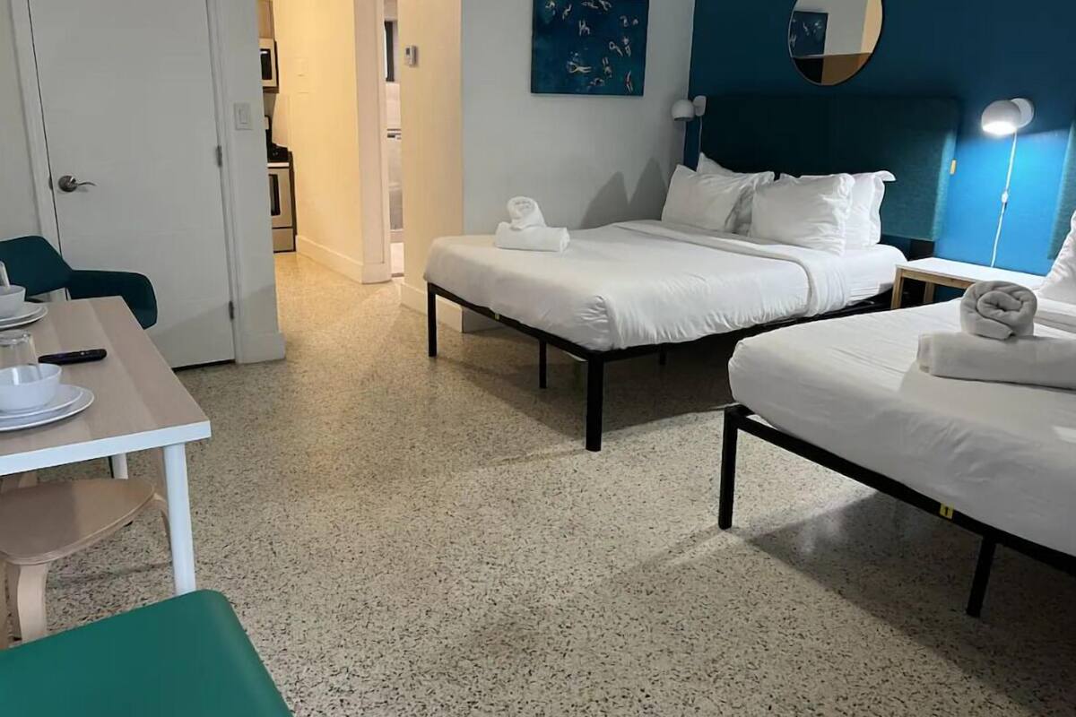 Een hotelkamer met twee bedden, een eettafel en een stoel. Er hangt een schilderij aan de muur en boven het bed is een spiegel.