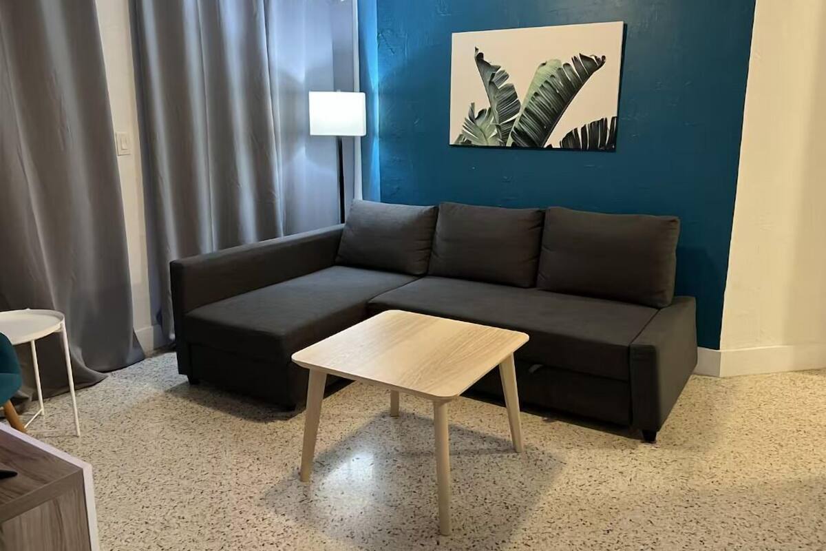 Een moderne woonkamer met een donkergrijze modulaire bank, een klein houten salontafel en een wanddecoratie van bladeren.