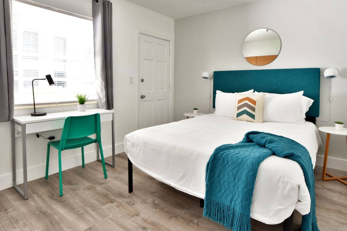 Een hotelkamer met een bed, bureau, stoel en een raam met gordijnen.