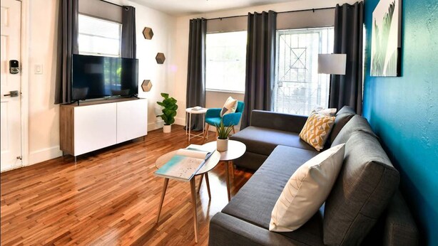 En moderne stue med et fladskærms-tv, en sofa, et sofabord og et lille sengebord.