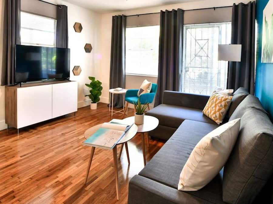 Una sala de estar moderna con un televisor de pantalla plana, un sofá, una mesa de centro y una mesita auxiliar.