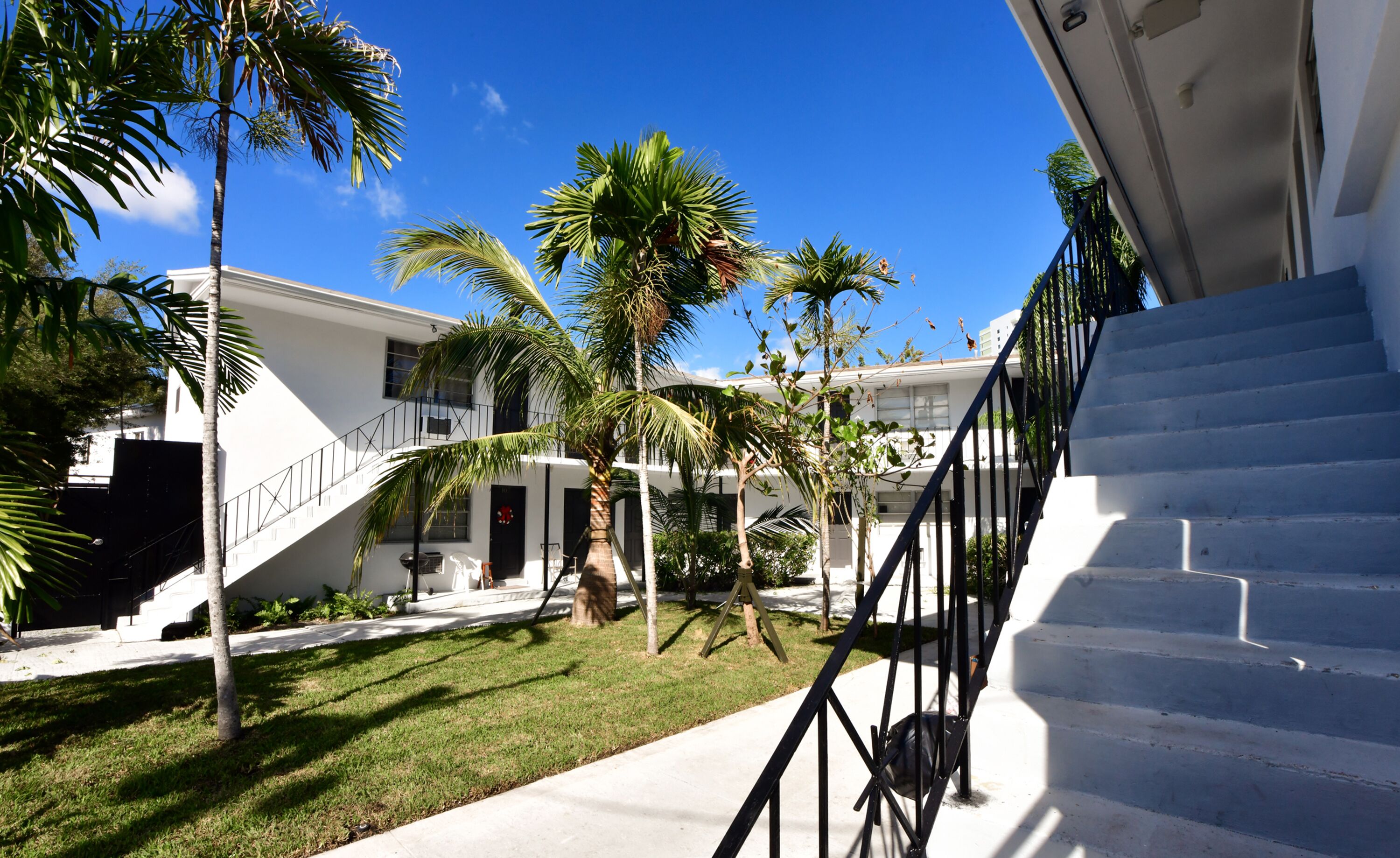 A white building with a staircase and palm trees in the yard.