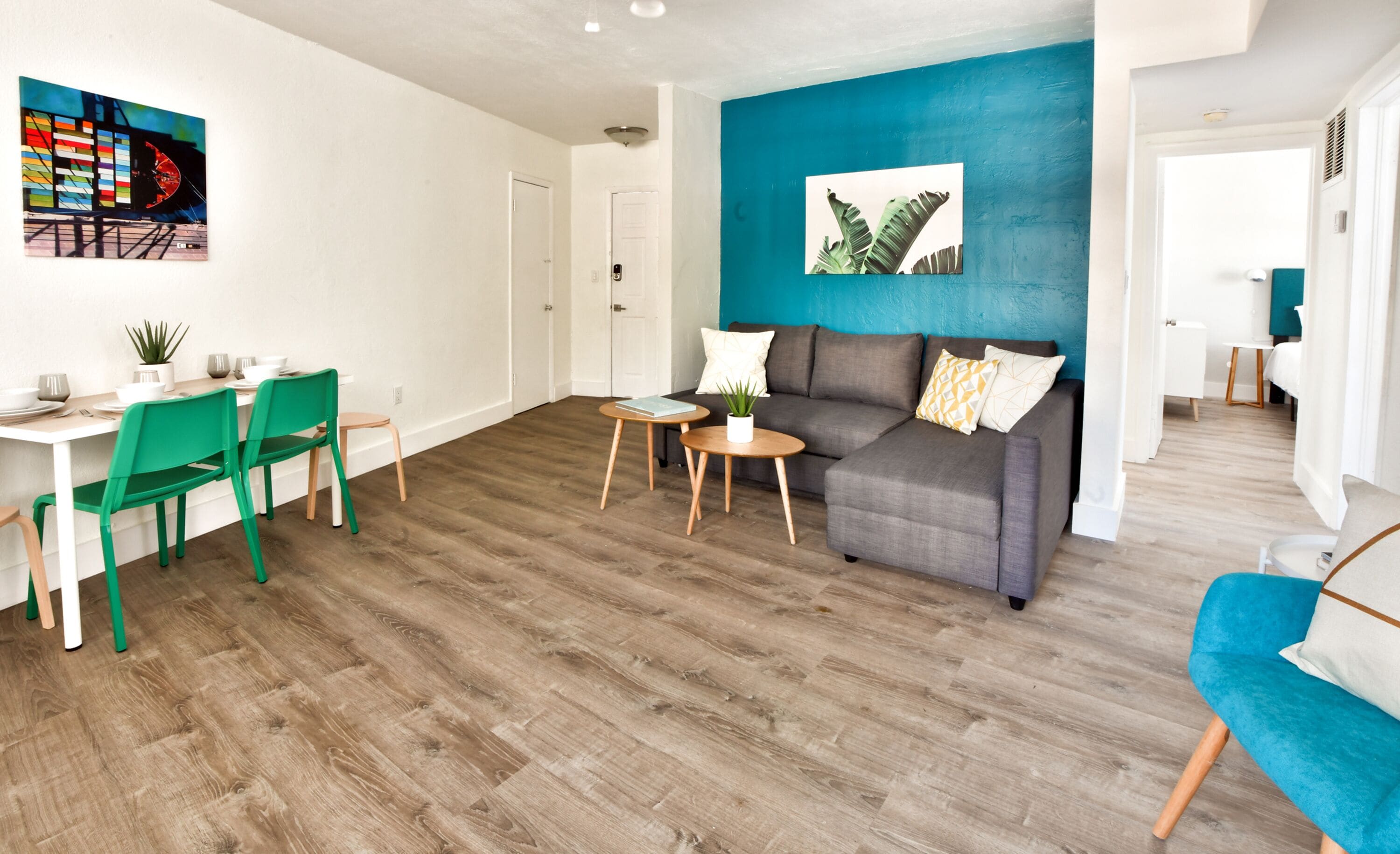 A modern living room with a dining area, a blue accent wall, and a wooden floor.