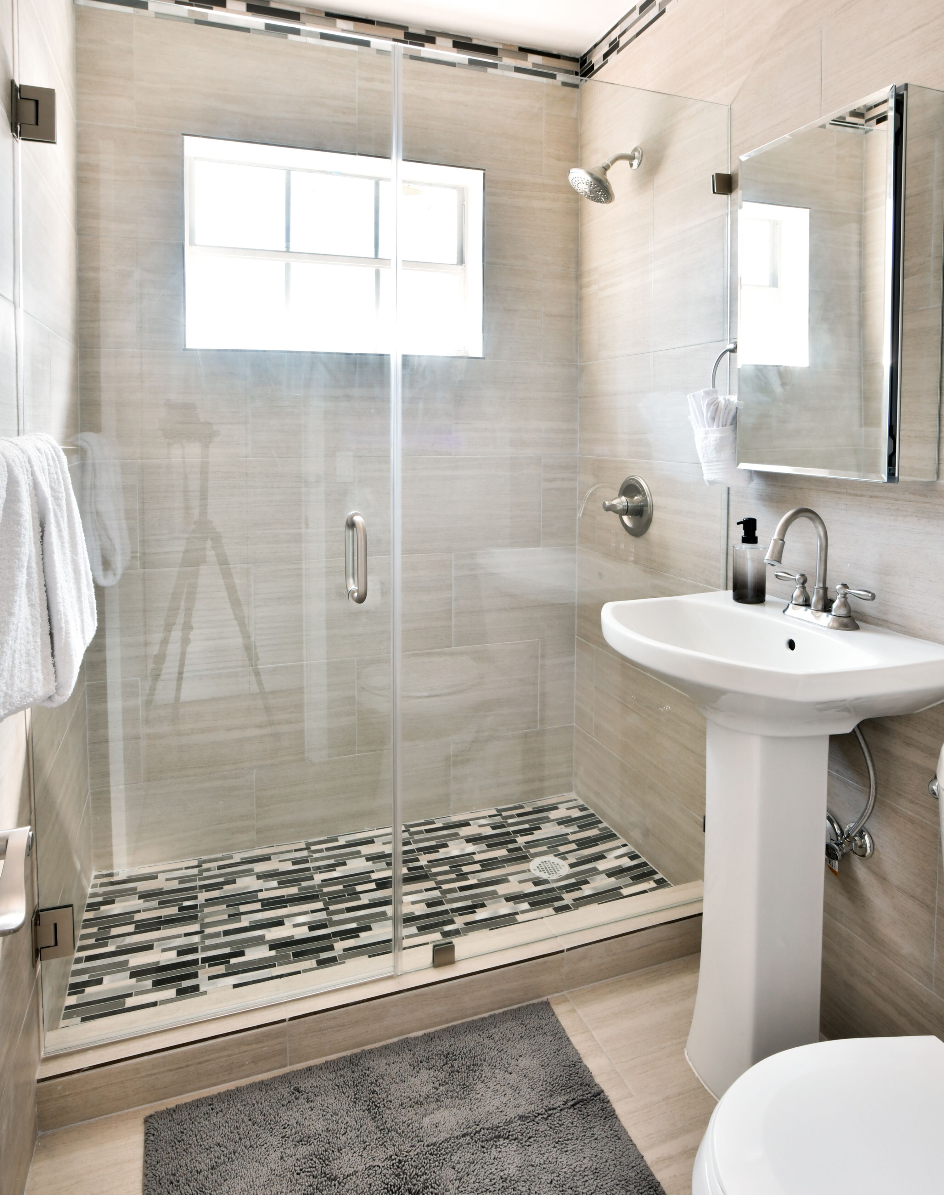 Un baño moderno con cabina de ducha de vidrio, un lavabo blanco y un espejo encima.