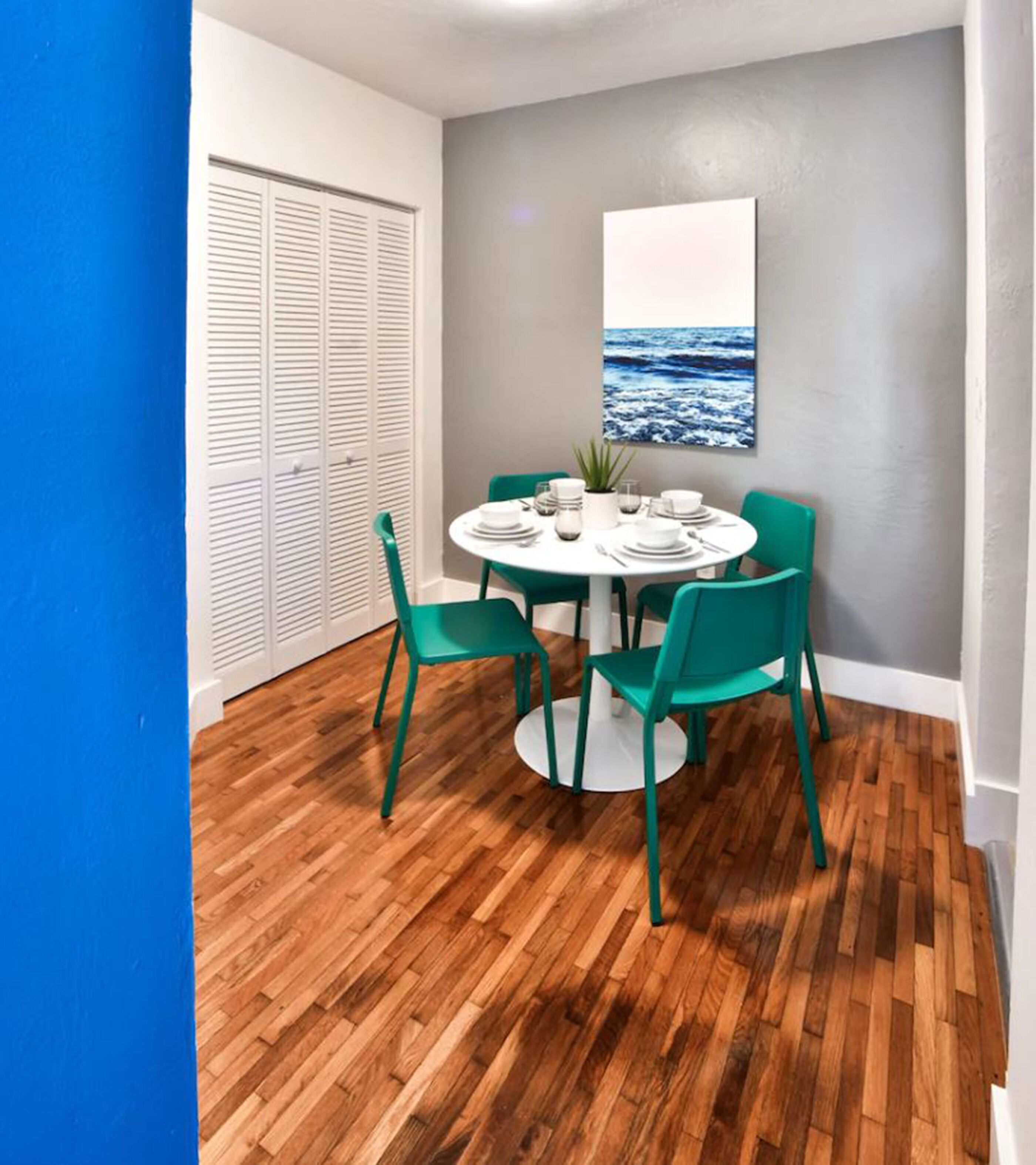 Uma área de refeições com uma mesa redonda, quatro cadeiras verdes e uma toalha de mesa branca.